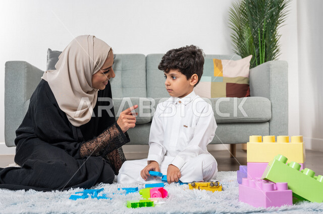 أم عربية خليجية سعودية محجبة تلعب مع طفلها، ممارسة الانشطة الترفيهية، ايماءات وجه سعيدة، مفهوم الأمومة والطفولة، أنشطة ترفيهية للطفل، رعاية الاطفال، تطوير مهارات الطفل، الاهتمام ودعم الأبناء
