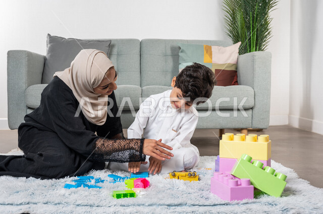 أم عربية خليجية سعودية محجبة تلعب مع طفلها، ممارسة الانشطة الترفيهية، ايماءات وجه سعيدة، مفهوم الأمومة والطفولة، أنشطة ترفيهية للطفل، رعاية الاطفال، تطوير مهارات الطفل، الاهتمام ودعم الأبناء