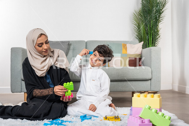 أم عربية خليجية سعودية محجبة تلعب مع طفلها، ممارسة الانشطة الترفيهية، ايماءات وجه تدل على السعادة، مفهوم الأمومة والطفولة، مفهوم الأمومة والطفولة، أنشطة ترفيهية للطفل، رعاية الاطفال، تطوير مهارات الطفل، الاهتمام ودعم الأبناء