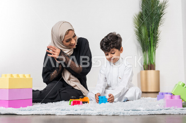 أم عربية خليجية سعودية محجبة تلعب مع طفلها الصغير، التشجيع والتحفيز، ايماءات وجه تدل على السعادة، مفهوم الأمومة والطفولة، أنشطة ترفيهية للطفل، رعاية الاطفال، تطوير مهارات الطفل، الاهتمام ودعم الأبناء