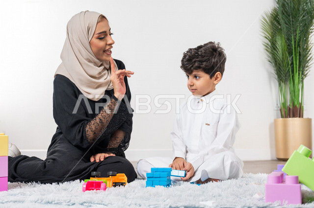 A veiled Saudi Gulf Arab mother plays with her child, practicing recreational activities, facial and hand gestures indicating happiness, the concept of motherhood and childhood, caring for children, children's entertainment activities, children's particip