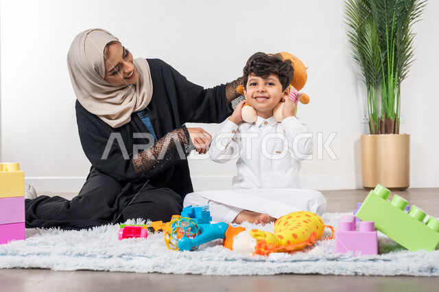 أم عربية خليجية سعودية محجبة تلعب مع طفلها، ممارسة الانشطة الترفيهية، ايماءات وجه تدل على السعادة، مفهوم الأمومة والطفولة، رعاية الاطفال، انشطة الاطفال الممتعة في المنزل، مشاركة الابناء الانشطة الترفيهية، أجواء عائلية سعيدة
