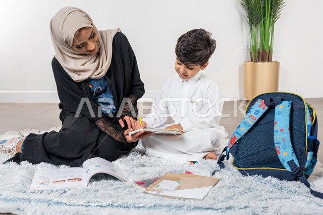 A Saudi Gulf Arab mother helps her child learn at home, educational activities, child development, encouragement and development of children, helping children with homework, school backpacks, caring and supporting children