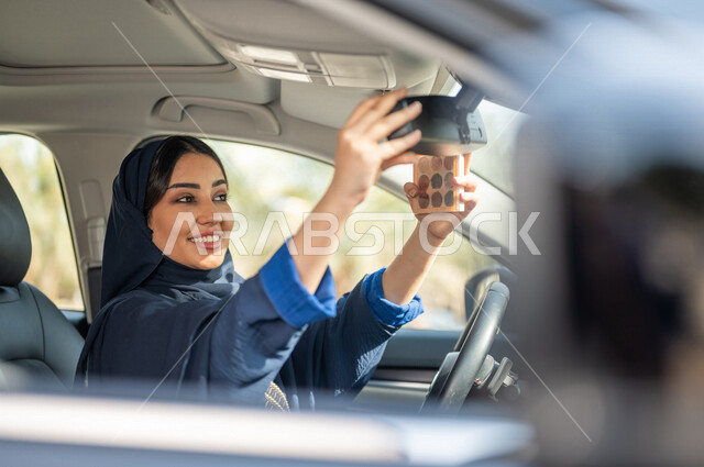 امرأه عربية خليجية سعودية محجبة تجلس في السيارة وتمسك بيدها احدى ادوات المكياج، قيادة المرأة، مرأة خبيرة بمستحضرات التجميل، مفهوم الإهتمام بالجمال والبشرة، ادوات مكياج تتوريال، حرية القيادة للمرأة السعودية