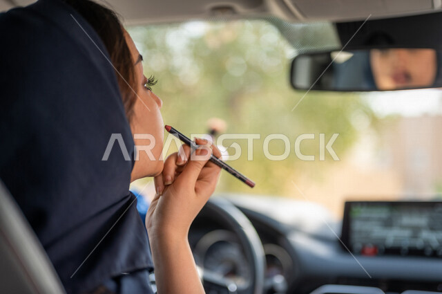 امرأه عربية خليجية سعودية محجبة تجلس في السيارة وتقوم بتزيين وجهها باستخدام احدى ادوات المكياج، قيادة المرأة، مرأة خبيرة بمستحضرات التجميل، مفهوم الإهتمام بالجمال والبشرة، ادوات مكياج تتوريال، حرية القيادة للمرأة السعودية
