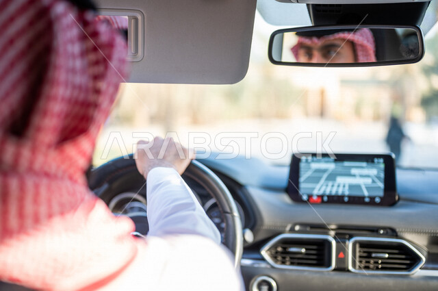 صورة من الخلف لرجل عربي خليجي سعودي يقود السيارة، انعكاس وجه السائق على المرآة، خدمة توصيل الركاب، خدمات النقل الامنة، دروس تعليم قيادة السيارات، سيارة الاجرة، قيادة السيارات