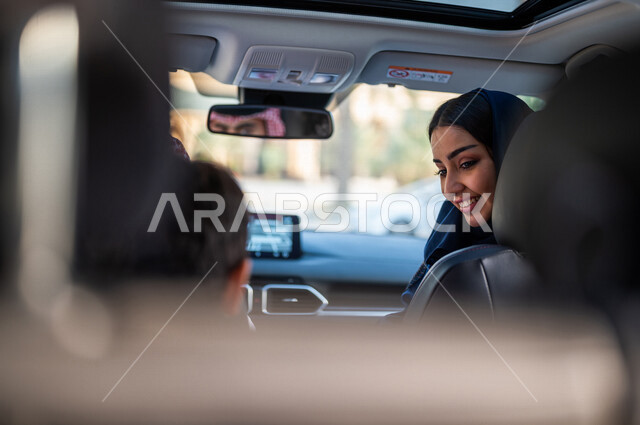 عائلة عربية خليجية سعودية تستمع برحلة في السيارة، انعكاس صورة رجل يقود السيارة على المرآة، امرأة تنظر الى الخلف، خدمة توصيل الركاب، خدمات النقل الامنة، دروس تعليم قيادة السيارات، ايماءات وجه مبتسمة، سيارة الاجرة، قيادة السيارات