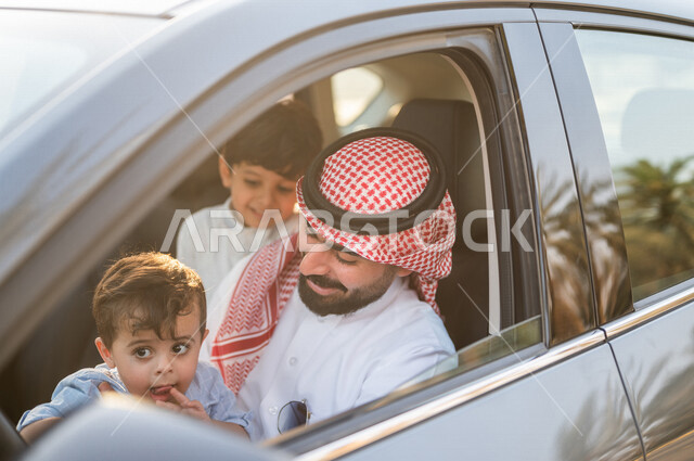 A close-up of a Saudi Arabian Gulf man sitting inside the car and playing with his child happily, passenger delivery service, safe transportation services, facial and hand gestures indicating happiness, taxi, driving cars