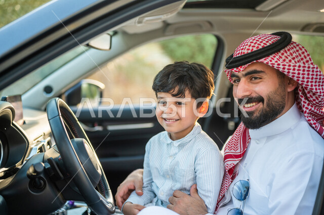 عائلة عربية خليجية سعودية تستمع برحلة في السيارة، اب يحمل ابنه وينظر نحو الكاميرا  بسعادة، خدمة توصيل الركاب، خدمات النقل الامنة، ايماءات وجه ويدين تدل على السعادة، سيارة الاجرة، قيادة السيارات