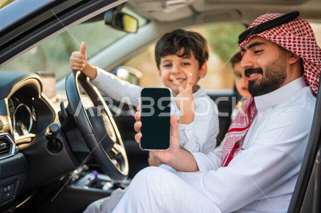 عائلة عربية خليجية سعودية تستمع برحلة في السيارة، عرض خدمات وتطبيقات الهاتف المحمول، تحديد الموقع، شاشة سوداء فارغة، طفل يرفع اصبع الابهام بايماءات تدل على الاعجاب والحماس، خدمة النقل من خلال تطبيق التوصيل