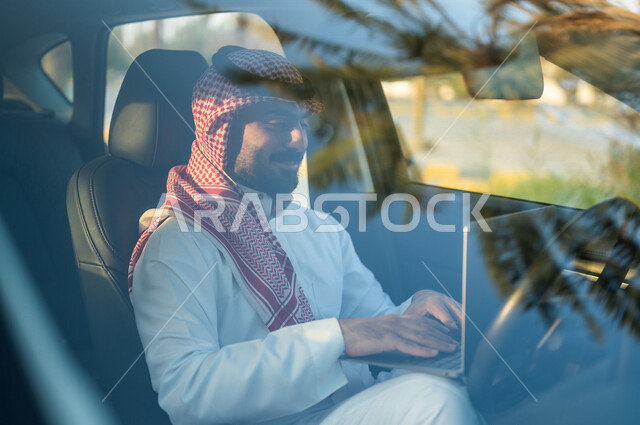 A Saudi Arabian Gulf man sitting in the car and using a laptop, surfing the Internet, working remotely, using social media, e-marketing, using modern technologies