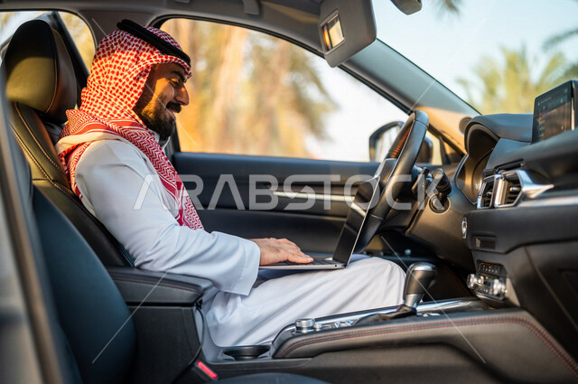 رجل عربي خليجي سعودي يجلس بالسيارة ويستخدم الحاسوب المحمول، تصفح الإنترنت، العمل عن بعد، إستخدام وسائل التواصل الإجتماعي، التسويق الإلكتروني، استخدام تقنيات حديثة