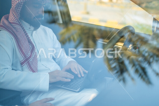 رجل عربي خليجي سعودي يجلس بالسيارة ويستخدم الحاسوب المحمول، تصفح الإنترنت، العمل عن بعد، إستخدام وسائل التواصل الإجتماعي، التسويق الإلكتروني، استخدام تقنيات حديثة