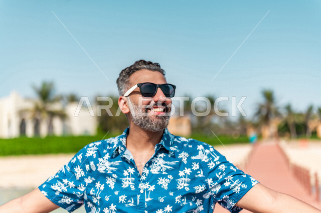 صوره مقربه لرجل عربي سعودي خليجي في رحله صيفيه ممتعه, أنشطه ترفيهيه, جوله على شاطيء بحر جده, الفعاليات الصيفيه, الإسترخاء والإستجمام, الشعور بالسعاده, عطلات سياحيه, منتجع سياحي, ارتداء الملابس الكاجوال الصيفيه, السياحه في السعوديه