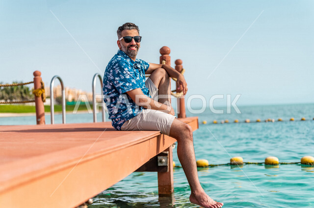 رجل عربي سعودي خليجي في رحله صيفيه ممتعه, عطله صيفيه, أنشطه ترفيهيه, الجلوس على شاطيء بحر جده, الفعاليات الصيفيه, الإسترخاء والإستجمام, الشعور بالسعاده, عطلات سياحيه, منتجع سياحي, ارتداء الملابس الكاجوال الصيفيه, السياحه في السعوديه