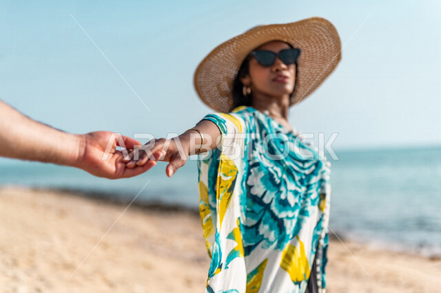 إمراه عربيه سعوديه خليجيه تمسك بيد زوجها على شاطيء البحر, أجواء رومانسيه, عطلة متزوجين في شهر العسل, وجهات سياحيه في شهر العسل، المشي على رمال البحر، سياحة وإستجمام، أناقه شاطئيه ملونه, الإجازه الصيفيه 