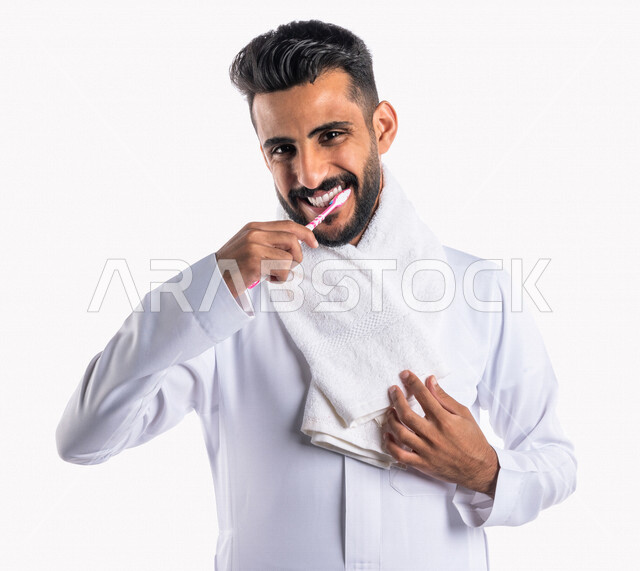 بورتريه بصورة مقربة لرجل عربي خليجي سعودي ، يقوم بتنظيف الأسنان بفرشاة الأسنان ، مفهوم العناية والإهتمام بصحة ونظافة الأسنان ، روتين نظافة الفم اليومية ، تجنب تسوس الاسنان وامراض اللثة ، خلفية بيضاء