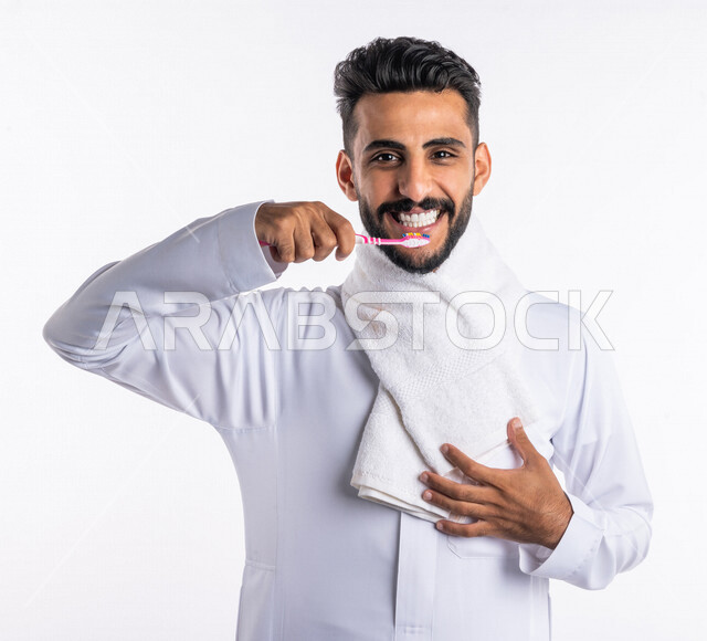 بورتريه بصورة مقربة لرجل عربي خليجي سعودي ، يقوم بتنظيف الأسنان بفرشاة الأسنان ، مفهوم العناية والإهتمام بصحة ونظافة الأسنان ، روتين نظافة الفم اليومية ، تجنب تسوس الاسنان وامراض اللثة ، خلفية بيضاء