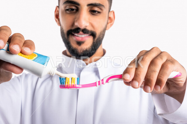 بورتريه بصورة مقربة لرجل عربي خليجي سعودي ، يقوم بتنظيف الأسنان بالفرشاة ومعجون الأسنان ، مفهوم العناية والإهتمام بصحة ونظافة الأسنان ، روتين نظافة الفم اليومية ، تجنب تسوس الاسنان وامراض اللثة ، خلفية بيضاء