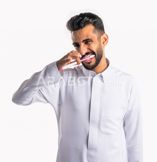 بورتريه بصورة مقربة لرجل عربي خليجي سعودي ، يقوم بتنظيف الأسنان بفرشاة الأسنان ، مفهوم العناية والإهتمام بصحة ونظافة الأسنان ، روتين نظافة الفم اليومية ، تجنب تسوس الاسنان وامراض اللثة ، خلفية بيضاء