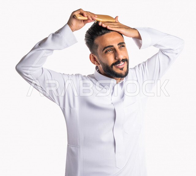 بورتريه بصورة مقربة لرجل عربي خليجي سعودي ، يقوم بتصفيف شعرة بفرشاة الشعر ( المشط ) ، تعابير تدل على السعادة ، مفهوم العناية و الإهتمام بالجمال و المظهر الخارجي ، خلفية بيضاء