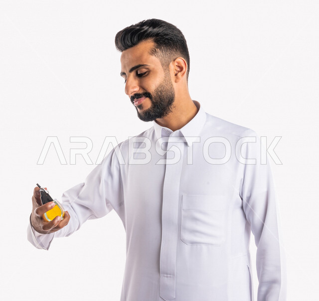 A close-up portrait of a Saudi Arabian Gulf man, applying perfume, perfuming and perfuming, the concept of elegance and attention to the external appearance, perfumes with luxurious and unique scents, festive occasions and weddings, white background, mark