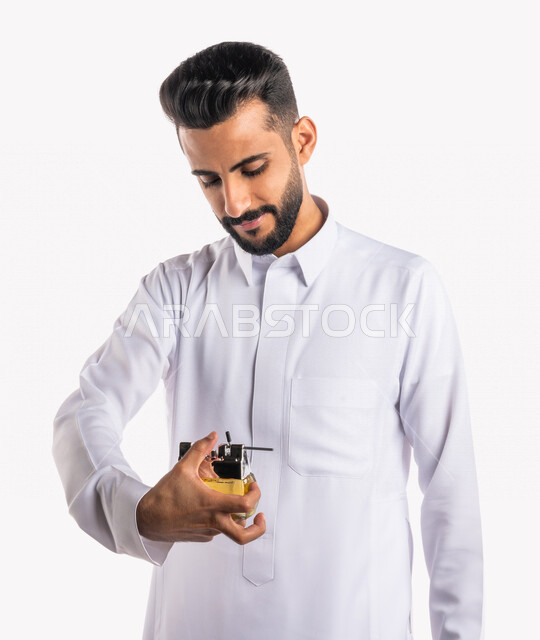 بورتريه بصورة مقربة لرجل عربي خليجي سعودي، يقوم بوضع العطر، التطيب والتعطر، مفهوم الأناقة والإهتمام المظهر الخارجي، عطور ذات روائح فاخرة وفريدة، مناسبات الأعياد وحفلات الزفاف، خلفية بيضاء، التسويق لمنتجات العطور، العود العطري
