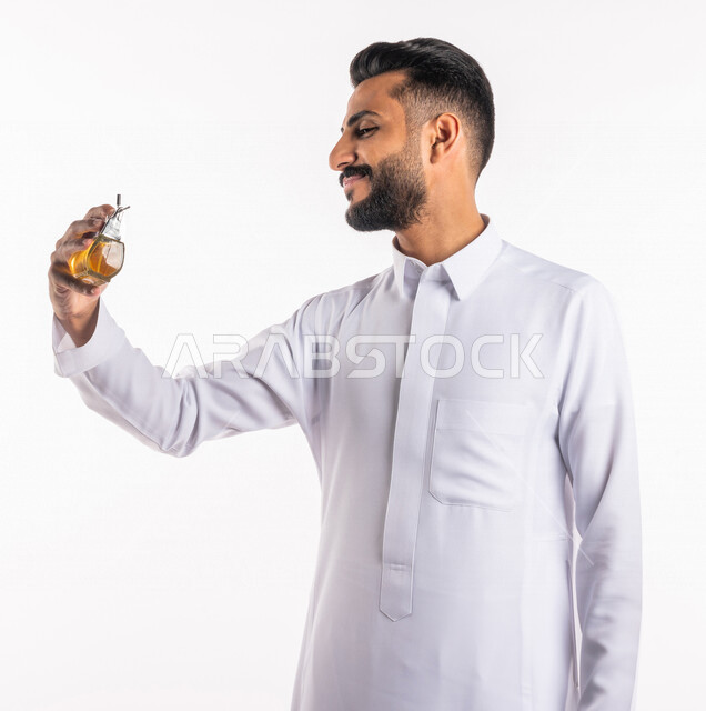بورتريه بصورة مقربة لرجل عربي خليجي سعودي، يقوم بوضع العطر، التطيب والتعطر، مفهوم الأناقة والإهتمام المظهر الخارجي، عطور ذات روائح فاخرة وفريدة، مناسبات الأعياد وحفلات الزفاف، خلفية بيضاء، التسويق لمنتجات العطور، العود العطري