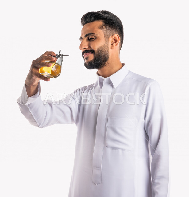 بورتريه بصورة مقربة لرجل عربي خليجي سعودي، يقوم بوضع العطر، التطيب والتعطر، مفهوم الأناقة والإهتمام المظهر الخارجي، عطور ذات روائح فاخرة وفريدة، مناسبات الأعياد وحفلات الزفاف، خلفية بيضاء، التسويق لمنتجات العطور، العود العطري