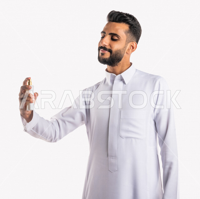 بورتريه بصورة مقربة لرجل عربي خليجي سعودي، يقوم بوضع العطر، التطيب والتعطر، مفهوم الأناقة والإهتمام المظهر الخارجي، عطور ذات روائح فاخرة وفريدة، مناسبات الأعياد وحفلات الزفاف، خلفية بيضاء، التسويق لمنتجات العطور، العود العطري