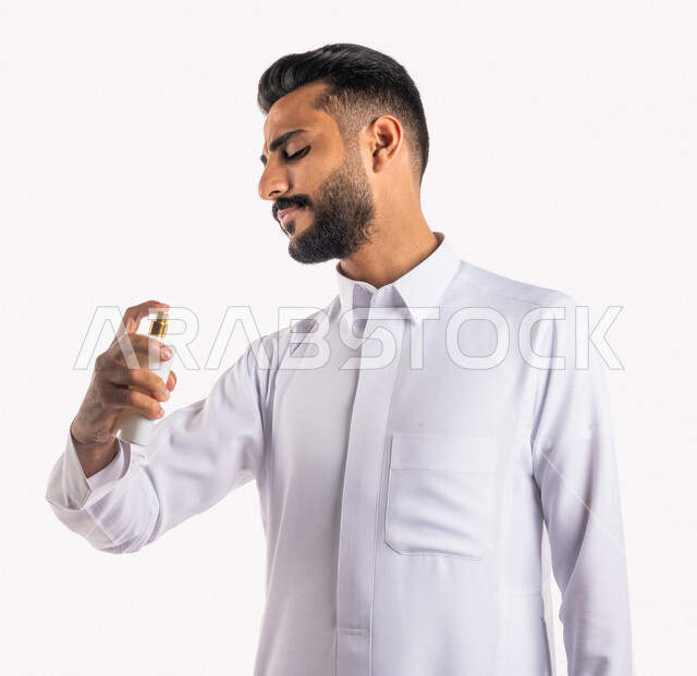 بورتريه بصورة مقربة لرجل عربي خليجي سعودي، يقوم بوضع العطر، التطيب والتعطر، مفهوم الأناقة والإهتمام المظهر الخارجي، عطور ذات روائح فاخرة وفريدة، مناسبات الأعياد وحفلات الزفاف، خلفية بيضاء، التسويق لمنتجات العطور، العود العطري