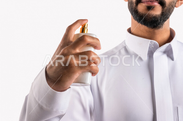 بورتريه بصورة مقربة لرجل عربي خليجي سعودي، يقوم بوضع العطر، التطيب والتعطر، مفهوم الأناقة والإهتمام المظهر الخارجي، عطور ذات روائح فاخرة وفريدة، مناسبات الأعياد وحفلات الزفاف، خلفية بيضاء، التسويق لمنتجات العطور، العود العطري
