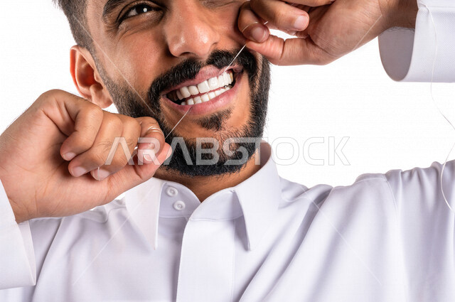 بورتريه بصورة مقربة لرجل عربي خليجي سعودي ، يقوم بإستخدام خيط تنظيف الأسنان ، مفهوم العناية والإهتمام بصحة الأسنان ، معدات طب الأسنان ، خلفية بيضاء