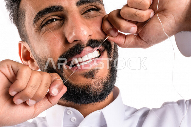 بورتريه بصورة مقربة لرجل عربي خليجي سعودي ، يقوم بإستخدام خيط تنظيف الأسنان ، مفهوم العناية والإهتمام بصحة الأسنان ، معدات طب الأسنان ، خلفية بيضاء