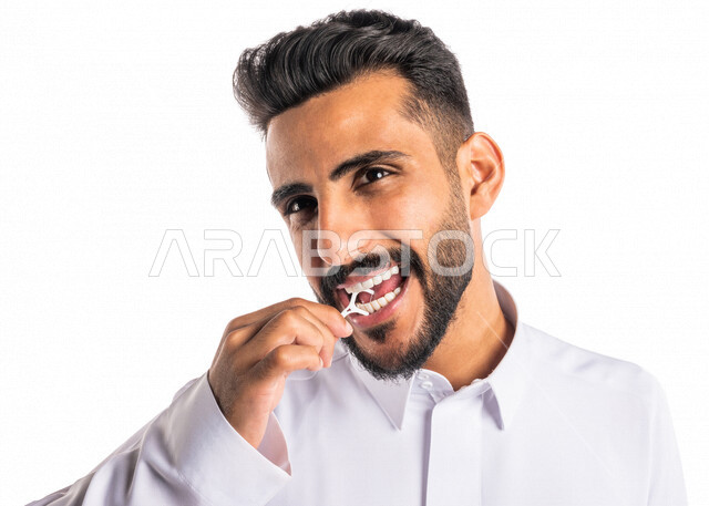 بورتريه بصورة مقربة لرجل عربي خليجي سعودي ، يقوم بإستخدام نكاشة تنظيف الأسنان بالخيط ، مفهوم العناية والإهتمام بصحة الأسنان ، معدات طب الأسنان ، خيط تنظيف الأسنان الطبي ، خلفية بيضاء