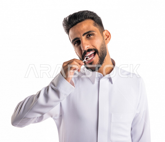 بورتريه بصورة مقربة لرجل عربي خليجي سعودي ، يقوم بإستخدام نكاشة تنظيف الأسنان بالخيط ، مفهوم العناية والإهتمام بصحة الأسنان ، معدات طب الأسنان ، خيط تنظيف الأسنان الطبي ، خلفية بيضاء