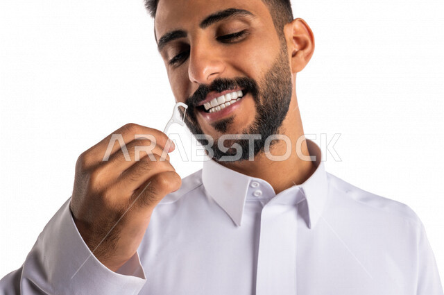 بورتريه بصورة مقربة لرجل عربي خليجي سعودي ، يقوم بإستخدام نكاشة تنظيف الأسنان بالخيط ، مفهوم العناية والإهتمام بصحة الأسنان ، معدات طب الأسنان ، خيط تنظيف الأسنان الطبي ، خلفية بيضاء
