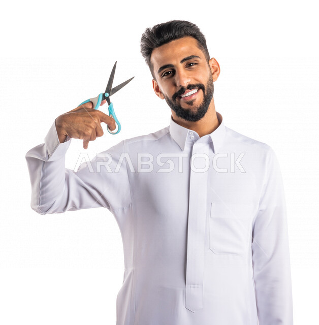 بورتريه لرجل عربي خليجي سعودي ، يحمل بيده المقص ، قص و تصفيف الشعر في صالون الحلاقة ، مفهوم العناية و الإهتمام بالجمال والمظهر الخارجي ، صالون حلاقة تجميلي رجالي ، خلفية بيضاء ، العناية والإهتمام بشعر صحي ونظيف