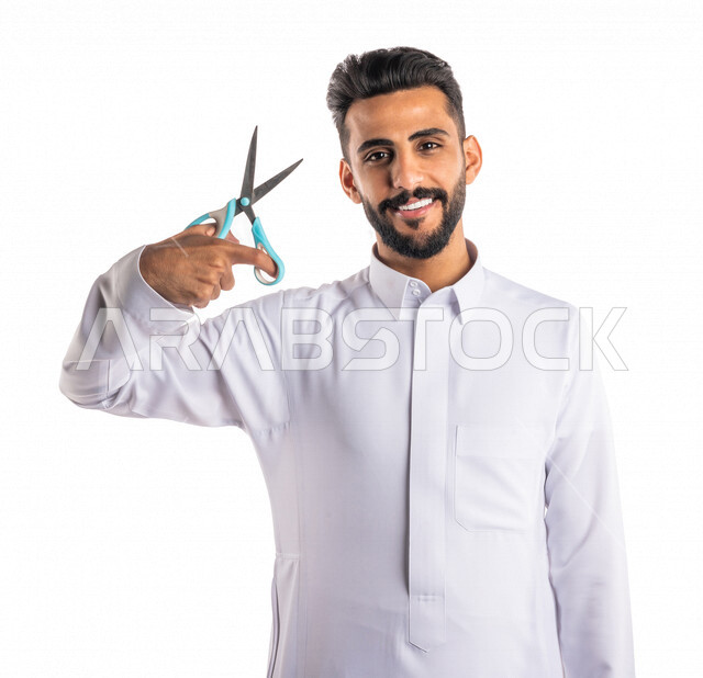 بورتريه لرجل عربي خليجي سعودي ، يحمل بيده المقص ، قص و تصفيف الشعر في صالون الحلاقة ، مفهوم العناية و الإهتمام بالجمال والمظهر الخارجي ، صالون حلاقة تجميلي رجالي ، خلفية بيضاء ، العناية والإهتمام بشعر صحي ونظيف