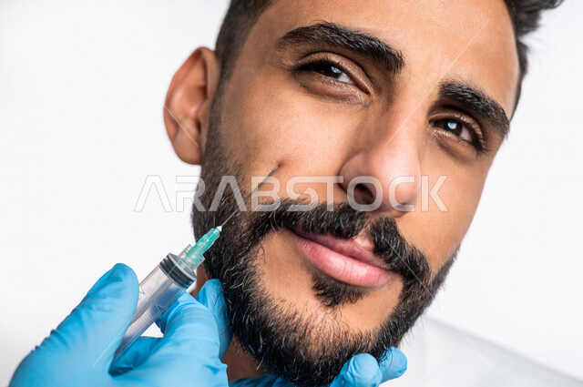 بورتريه بصورة مقربة ليد أخصائي يقوم بحقن مادة البوتوكس على وجه رجل عربي خليجي سعودي، مفهوم العناية والإهتمام بنضارة وتحسين البشرة، جلسات العناية بالبشرة، مكافحة الشيخوخة، عيادة تجميلية رجالية، علاج تجاعيد الوجه، حقن فيلر ( بوتوكس )