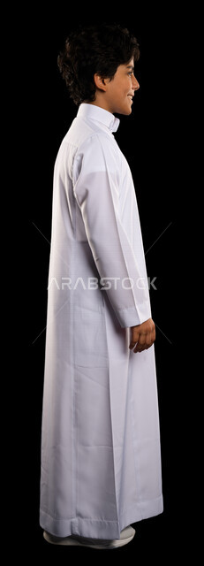 بورتريه من الجنب لولد عربي سعودي خليجي يرتدي الثوب السعودي، يقف بإستقامه، الوقوف بثقه، صوره للجسم بالطول الكامل, كامل الجسم, خلفية سوداء