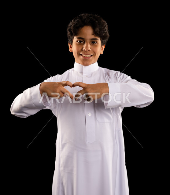 بورتريه لولد عربي سعودي خليجي يشكل بيده شكل القلب، إيماءات وجه ويدين تدل على الحب والفرح والسعادة، أعياد ومناسبات، الشعور بالحب والغرام, مناسبات سعيدة, خلفية سوداء