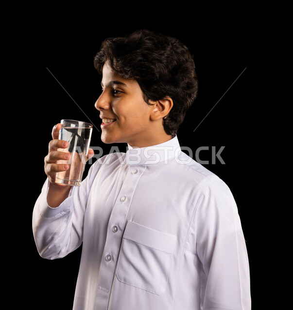 بورتريه لولد عربي خليجي سعودي يقوم بشرب الماء من كأس زجاجي، المحافظة على ترطيب الجسم, الإرتواء من العطش, تزويد الجسم بالطاقة، المداومه على شرب الماء, التخلص من سموم الجسم، خلفية سوداء, صحه ولياقه