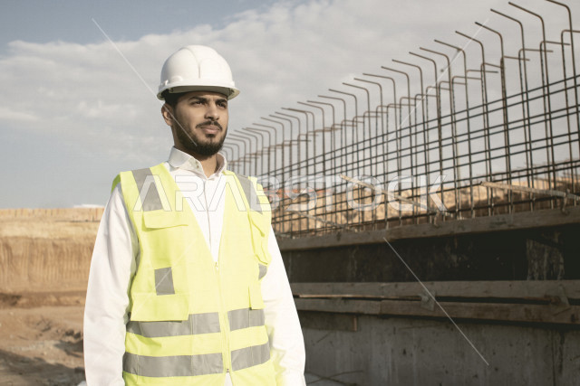 مقاول بناء عربي خليجي سعودي محترف في موقع البناء ، يرتدي سترة و خوذة الحماية ، العمل في موقع البناء ، انجاز الاعمال والمهام