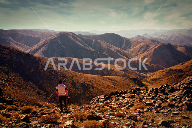 صورة من الخلف لسائح يمسك بيده كاميرا، الجبال والمرتفعات الرملية في المملكة العربية السعودية، مناظر طبيعية، الطبيعة الجبلية في السعودية، خلفية الطبيعة