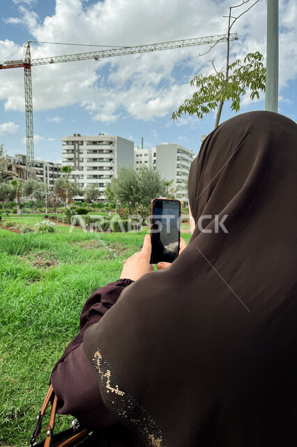 صورة مقربة لامرأة محجبة تحمل هاتف محمول، التقاط صور تذكارية، الاشجار والنباتات الخضراء في الحدائق العامة، جمال الطبيعة الخلابة، اماكن سياحية
