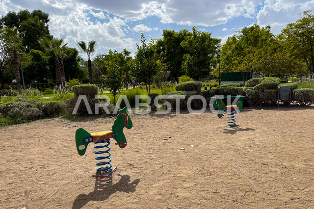 Empty horse-shaped swing in a public park, trees and green plants, children's swing, recreational activities, public gardens and parks, children's play area