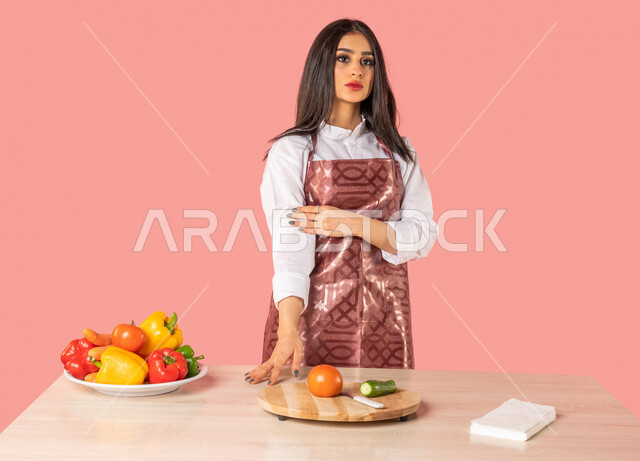 بورتريه لمرأة عربية، تقف أمام طاولة عليها مجموعة من الخضراوات الطازجة، إعداد السلطات والأطباق الصحية، مفهوم إتباع النظام الغذائي الصحي، ربة منزل، مفهوم الأكل الصحي، وجبة صحية، التدبير المنزلي، خلفية ملونة، خضراوات طازجة