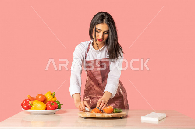 بورتريه لمرأة عربية، تقف أمام طاولة عليها مجموعة من الخضراوات الطازجة، إعداد السلطات والأطباق الصحية، مفهوم إتباع النظام الغذائي الصحي، ربة منزل، مفهوم الأكل الصحي، وجبة صحية، التدبير المنزلي، خلفية ملونة، خضراوات طازجة