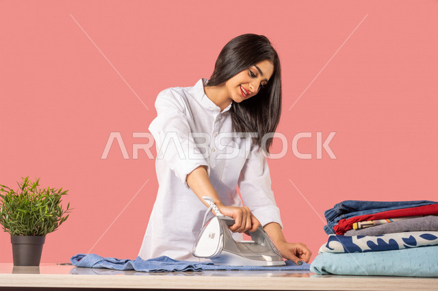 Portrait of an Arab woman, ironing clothes using an electric iron, ironing and organizing clothes, chores and chores, household electrical appliances, concept of ironing and drying clothes, colorful background, housewife, housekeeping